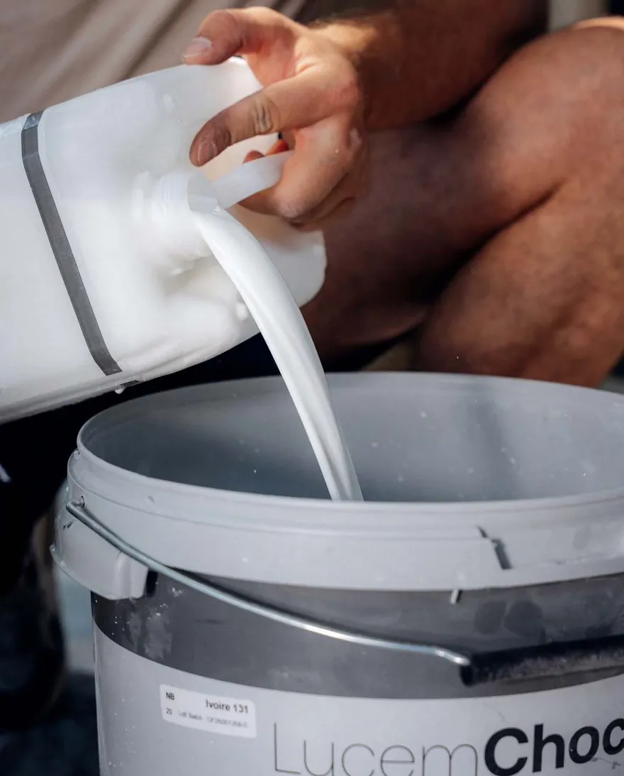 Un applicateur verse le composant liquide dans un seau de béton ciré LucemChoc