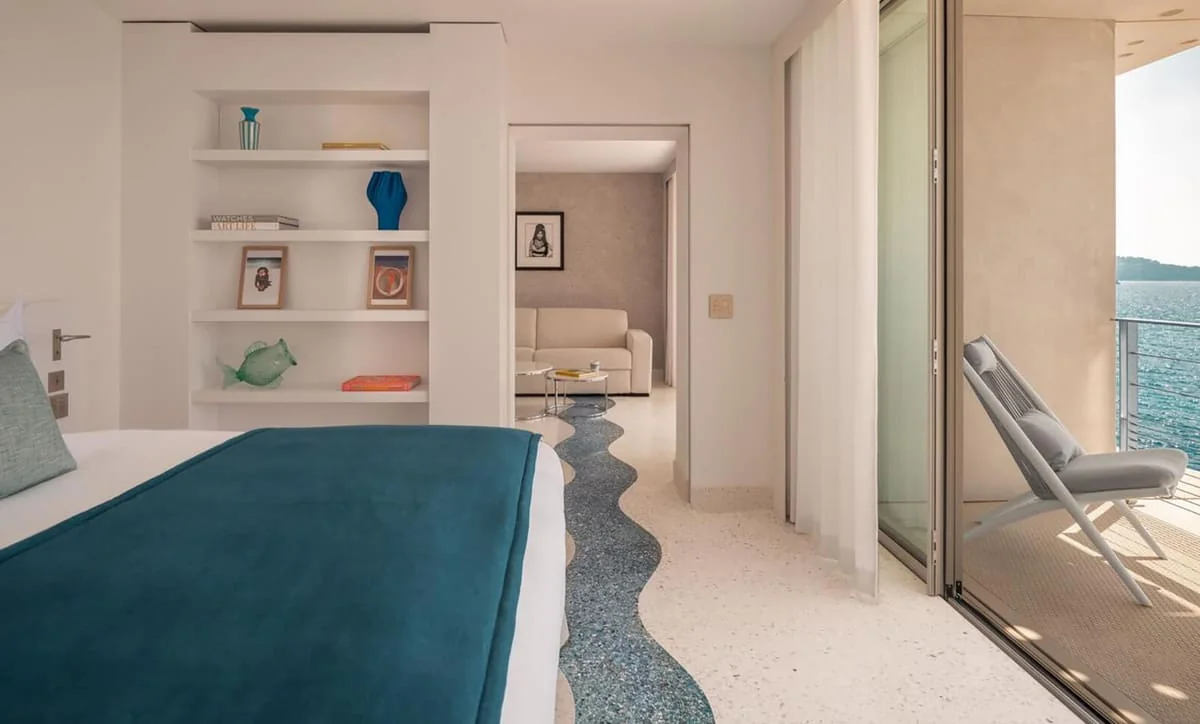 Suite de l'Hôtel Les Roches au Lavandou : sol en terrazzo LucemStone® traversé d'une vague de terrazzo bleu-gris, baie ouverte sur la Méditerranée